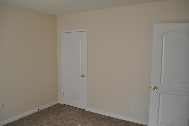 spare room featuring dark carpet and baseboards