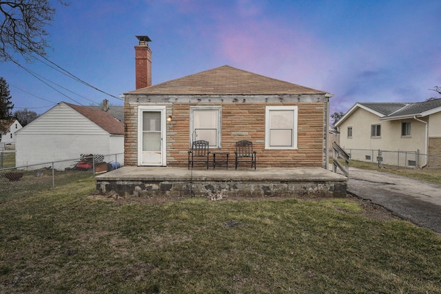 back of house at dusk with stone siding, fence, a patio, and a yard