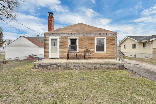 back of property with a lawn, a patio, stone siding, a chimney, and fence