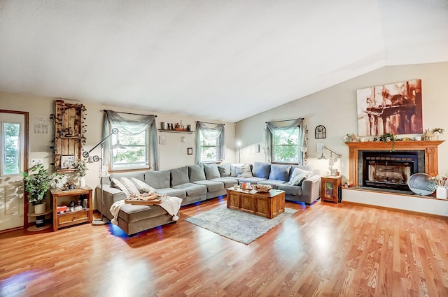 living area featuring vaulted ceiling, wood finished floors, and a fireplace with raised hearth