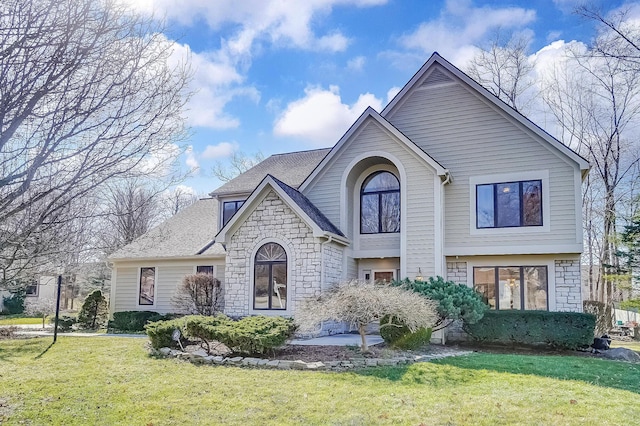 view of front of home featuring a front yard, stone siding, and a shingled roof