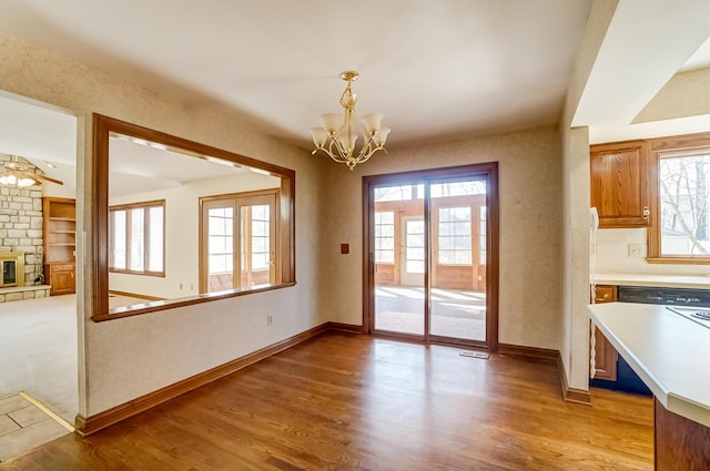 unfurnished dining area with baseboards, a notable chandelier, a stone fireplace, and light wood finished floors