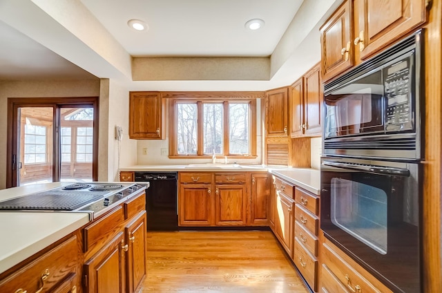 kitchen featuring light countertops, brown cabinets, light wood-style flooring, black appliances, and a sink