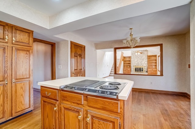 kitchen featuring baseboards, light wood finished floors, stainless steel electric cooktop, light countertops, and a notable chandelier