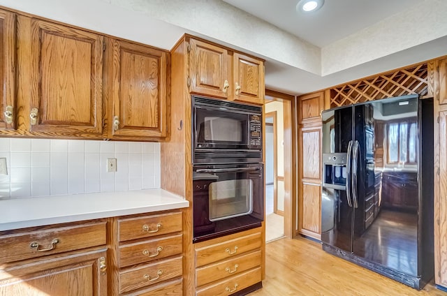 kitchen featuring light wood-type flooring, brown cabinets, black appliances, tasteful backsplash, and light countertops