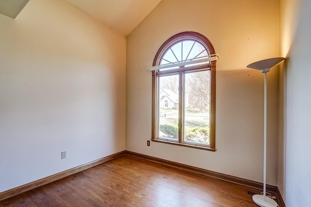 spare room with baseboards, wood finished floors, and vaulted ceiling