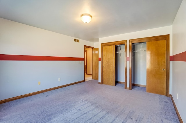 unfurnished bedroom featuring baseboards, visible vents, multiple closets, and carpet floors