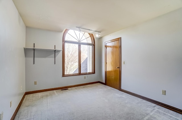 unfurnished room with rail lighting, light colored carpet, visible vents, and baseboards