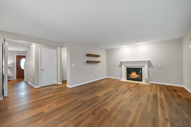 unfurnished living room with a fireplace with flush hearth, baseboards, and wood finished floors