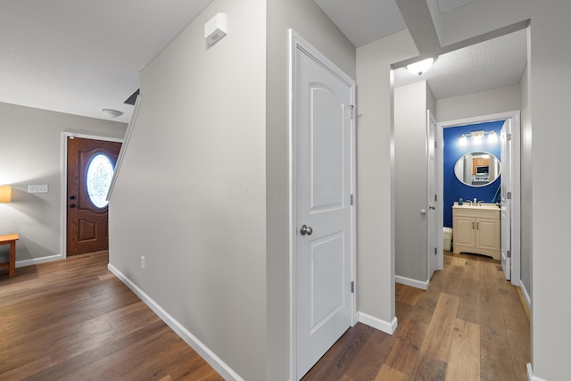 corridor featuring baseboards, a sink, and hardwood / wood-style floors