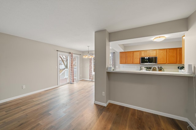 kitchen featuring baseboards, stainless steel microwave, brown cabinets, dark wood-style flooring, and an inviting chandelier