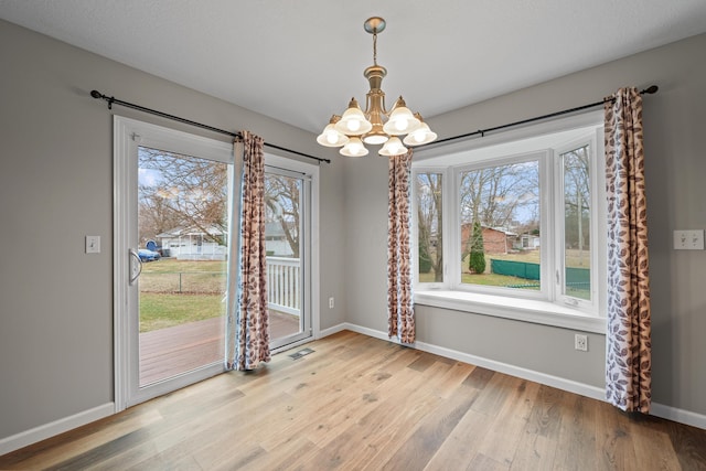 unfurnished dining area featuring a notable chandelier, visible vents, baseboards, and wood finished floors