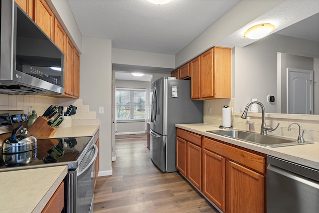 kitchen with light countertops, decorative backsplash, appliances with stainless steel finishes, a sink, and wood finished floors