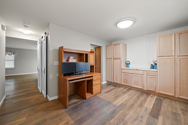 kitchen featuring a barn door, light countertops, wood finished floors, and light brown cabinetry