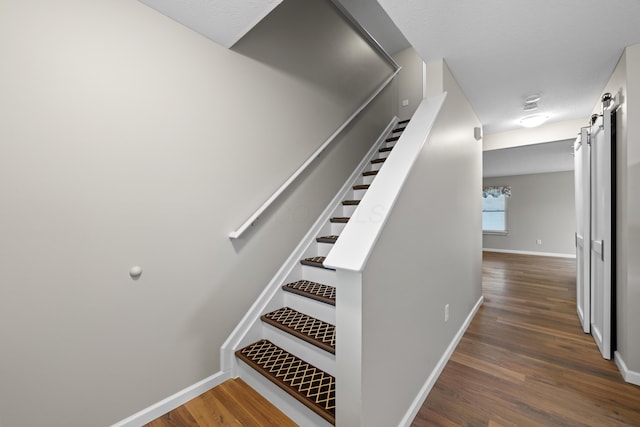 stairs featuring a barn door, baseboards, and wood finished floors