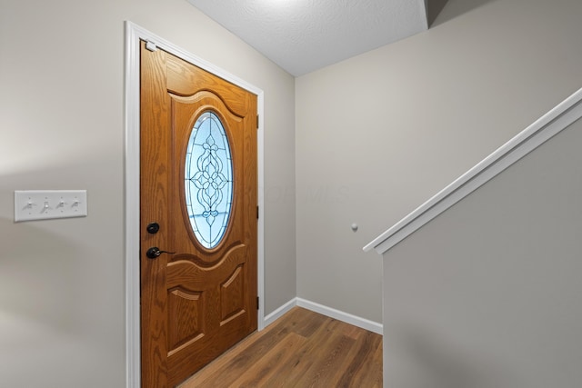 foyer entrance with a textured ceiling, baseboards, and wood finished floors