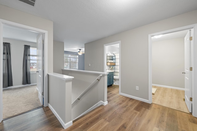 corridor featuring visible vents, a textured ceiling, an upstairs landing, wood finished floors, and baseboards