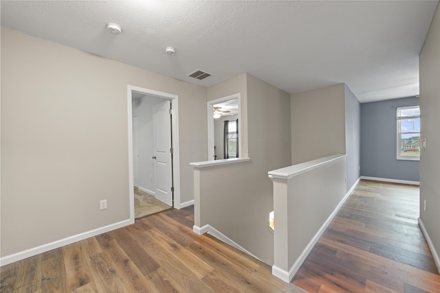 corridor with visible vents, wood finished floors, an upstairs landing, and a healthy amount of sunlight