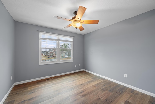 spare room with a ceiling fan, wood finished floors, visible vents, and baseboards