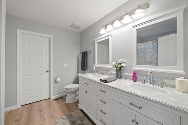 bathroom featuring wood finished floors, a sink, toilet, and double vanity