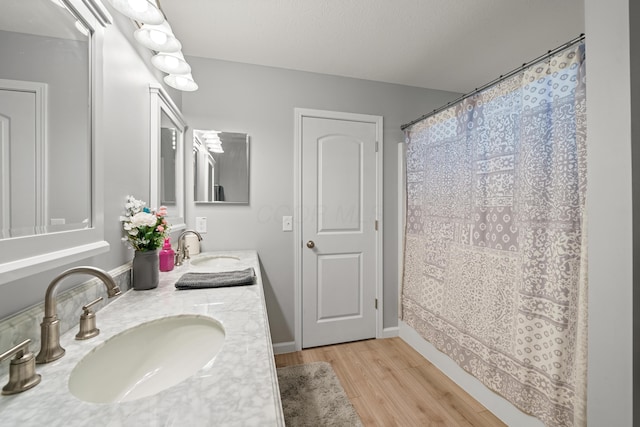 full bathroom featuring double vanity, baseboards, a sink, and wood finished floors