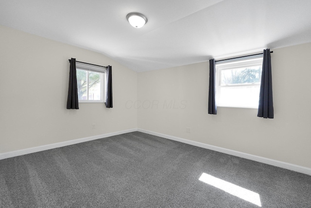 spare room featuring vaulted ceiling, dark carpet, and baseboards