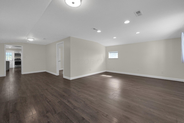 spare room with baseboards, visible vents, lofted ceiling, dark wood-type flooring, and recessed lighting