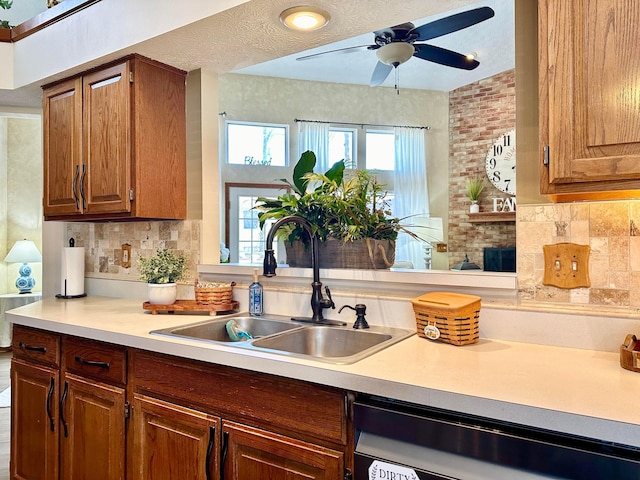 kitchen featuring light countertops, backsplash, brown cabinetry, a sink, and dishwashing machine