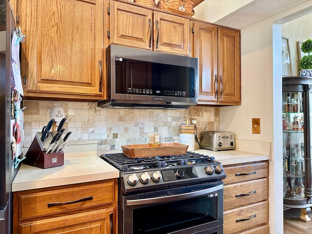 kitchen featuring appliances with stainless steel finishes, light countertops, brown cabinetry, and tasteful backsplash