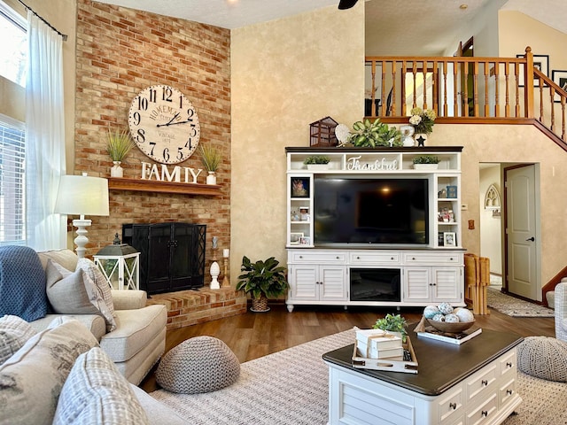 living area featuring a brick fireplace, dark wood finished floors, stairway, and a high ceiling