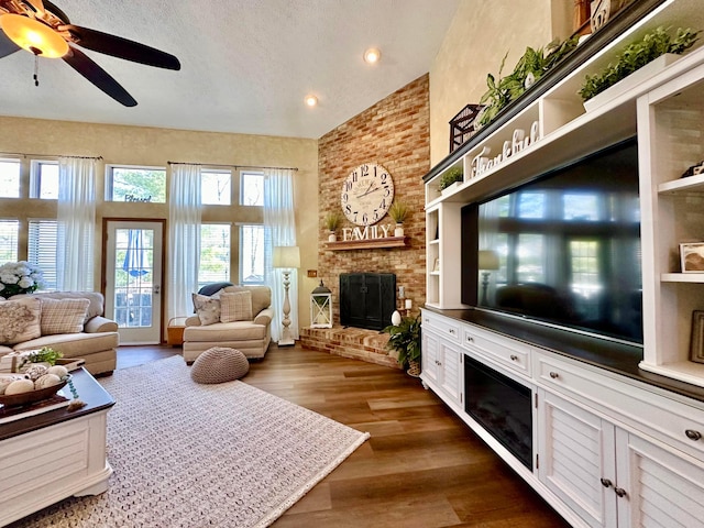 living room featuring a ceiling fan, a brick fireplace, a textured ceiling, wood finished floors, and high vaulted ceiling