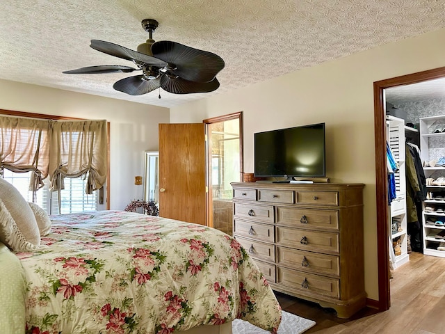 bedroom with a textured ceiling, a ceiling fan, a spacious closet, a closet, and light wood-type flooring