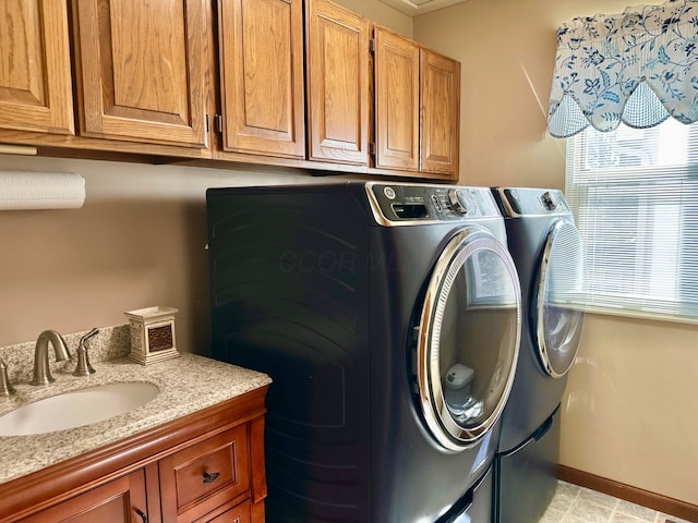 clothes washing area featuring separate washer and dryer, a sink, baseboards, cabinet space, and plenty of natural light