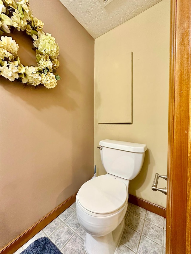 bathroom featuring a textured ceiling, tile patterned flooring, toilet, and baseboards