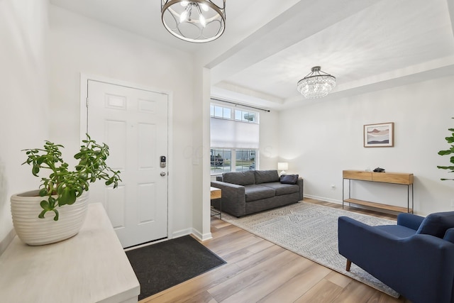 foyer with baseboards, a tray ceiling, light wood-style floors, and a notable chandelier