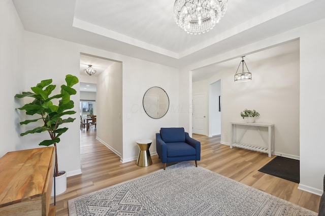 living area with a chandelier, a raised ceiling, baseboards, and wood finished floors