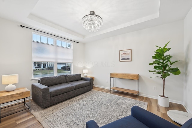 living room featuring an inviting chandelier, a raised ceiling, baseboards, and wood finished floors