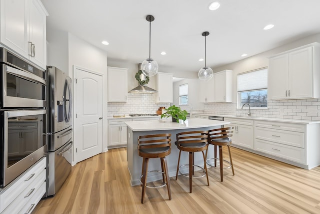 kitchen featuring white cabinets, a kitchen island, appliances with stainless steel finishes, a breakfast bar area, and light wood-style floors