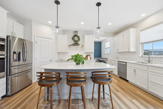 kitchen with appliances with stainless steel finishes, white cabinets, a sink, and wall chimney exhaust hood