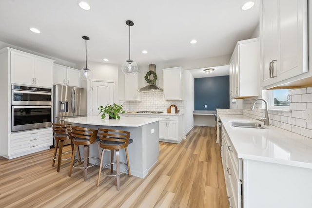 kitchen featuring a breakfast bar area, stainless steel appliances, wall chimney range hood, white cabinetry, and a sink