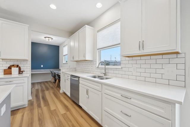 kitchen with light countertops, stainless steel dishwasher, white cabinetry, a sink, and light wood-type flooring