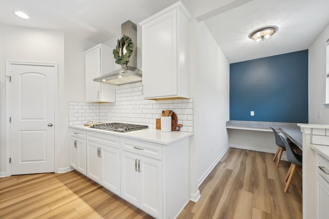 kitchen with white cabinets, light wood-style floors, decorative backsplash, wall chimney exhaust hood, and built in desk