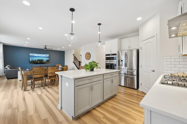 kitchen featuring a center island, light wood finished floors, stainless steel appliances, tasteful backsplash, and light countertops