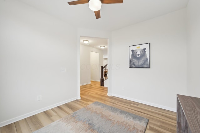 empty room with stairs, ceiling fan, light wood-type flooring, and baseboards