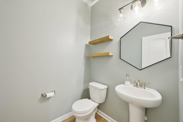 half bath featuring wood finished floors, a sink, toilet, and baseboards