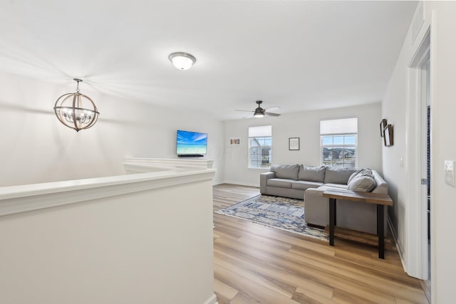 living area with light wood-type flooring, baseboards, and ceiling fan with notable chandelier