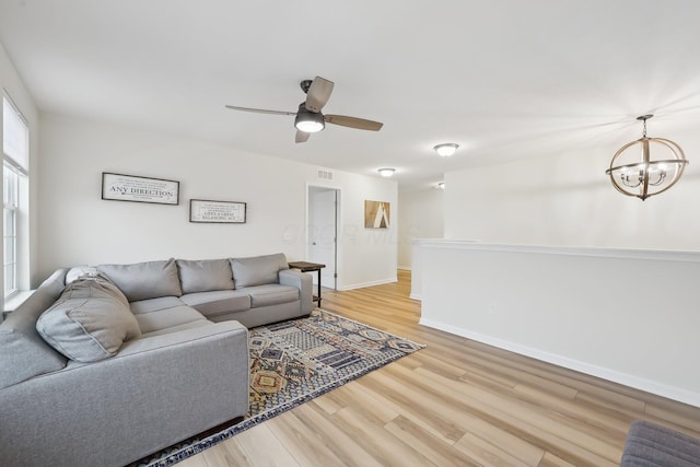 living room featuring ceiling fan with notable chandelier, wood finished floors, visible vents, and baseboards