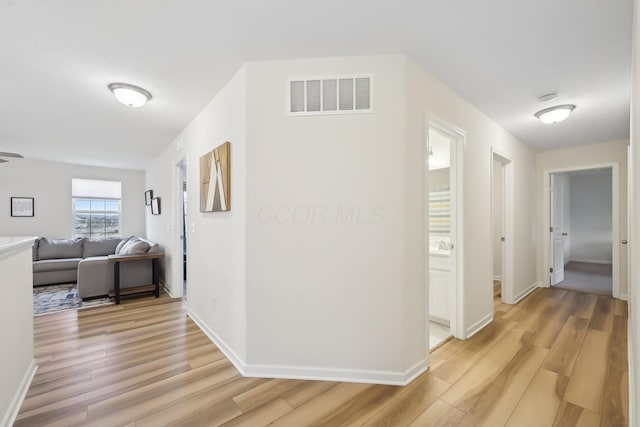 hallway with light wood finished floors, baseboards, and visible vents