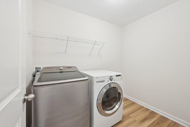 washroom with laundry area, light wood finished floors, washer and clothes dryer, and baseboards