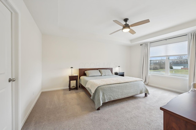 carpeted bedroom featuring a ceiling fan, a tray ceiling, and baseboards